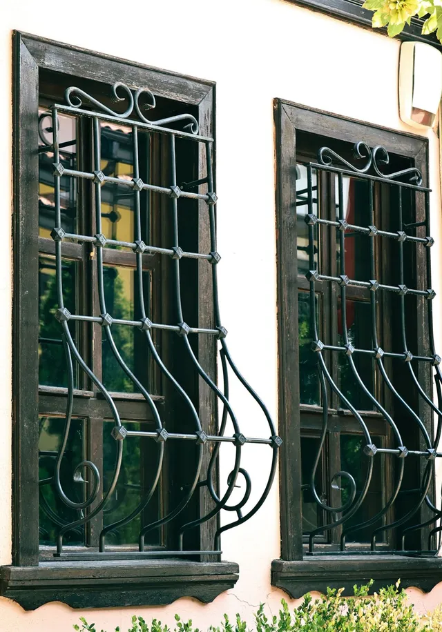 Dark-framed window fitted with a black wrought-iron grille, pale facade